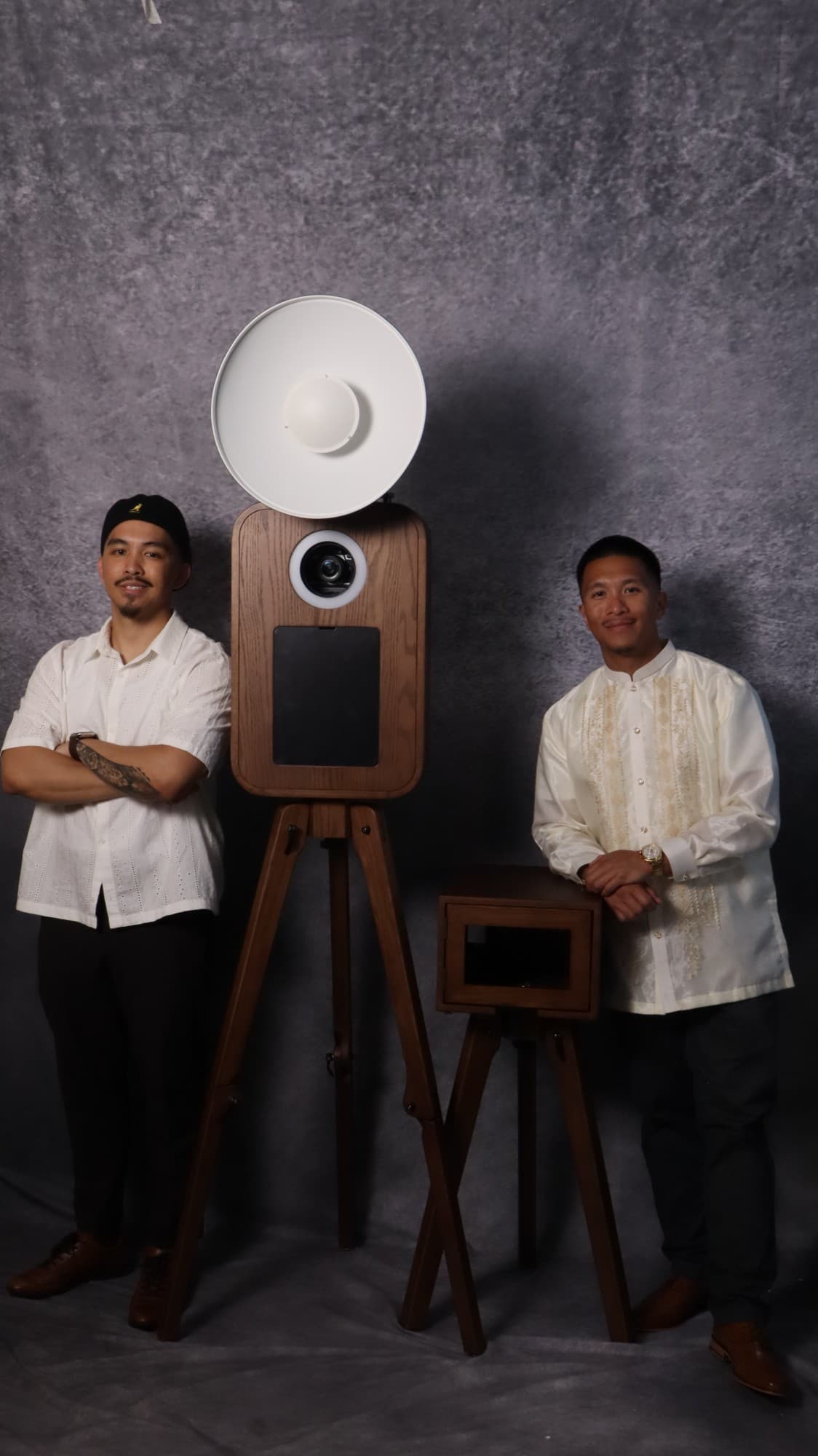 The two Katha founders standing beside their oak booth on a gray studio backdrop