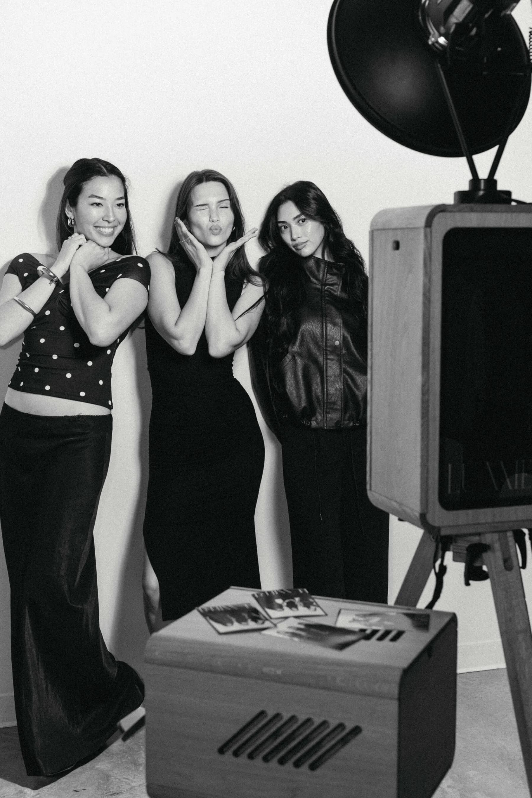 Three guests posing beside the oak booth, fresh prints on the case — high-contrast monochrome